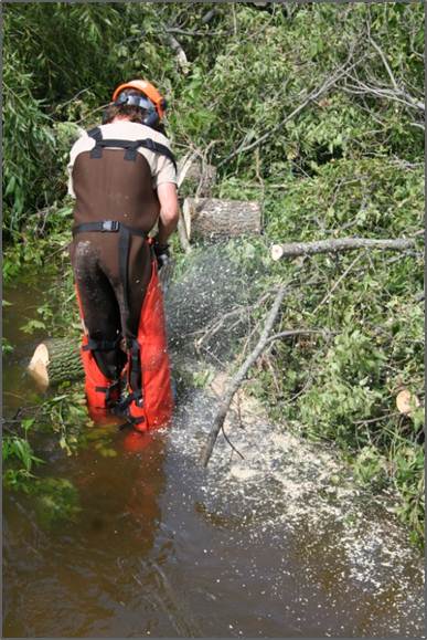 Man using chainsaw to cut out trees and branches from river 