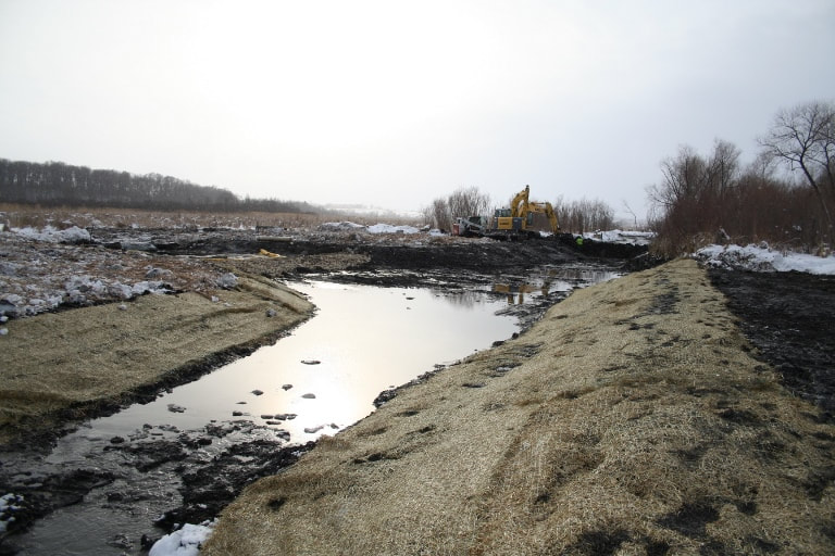 Construction of Kingston Wetland channel. Reinforced channel banks with some water, construction equipment in distance